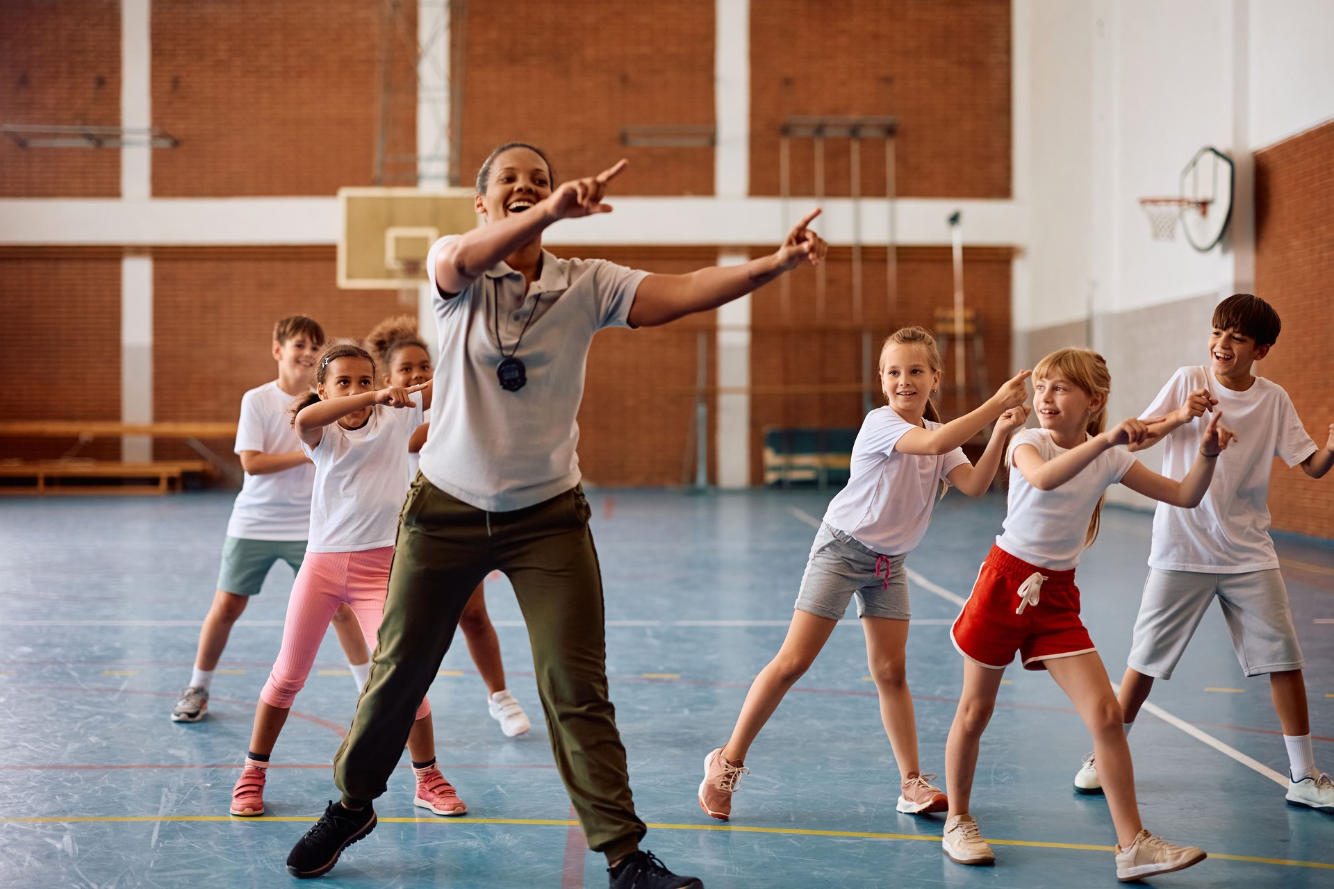 Group of happy school kids exercising with their coach during physical education class.